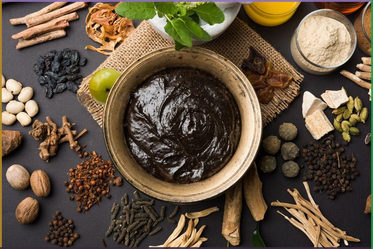 Ayurvedic herbal paste in a brass bowl surrounded by spices, amla, honey, and medicinal roots